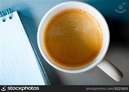 cup of coffee and notebook on table in blue light. Focus on mug