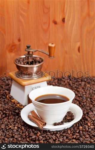 cup of coffee and roasted coffee beans with retro manual grinder, cinnamon