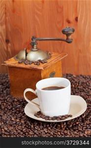 cup of coffee and roasted coffee beans with retro manual grinder near wooden wall