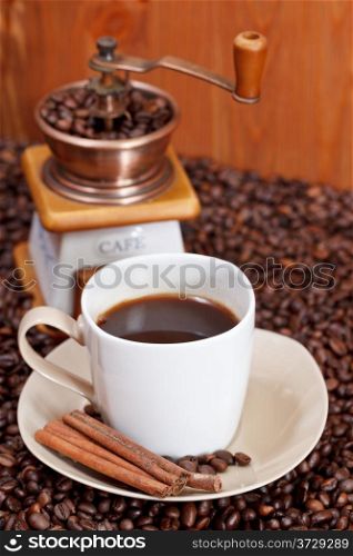 cup of coffee and roasted coffee beans with retro manual mill, cinnamon close up