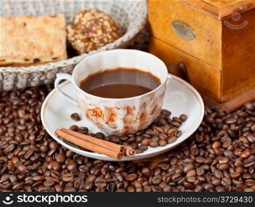 cup of coffee and roasted coffee beans with retro wooden manual mill, biscuit, cinnamon