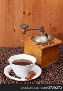 cup of coffee and roasted coffee beans with retro wooden manual mill, cinnamon