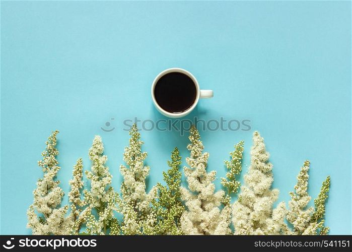 Cup of coffee and row blooming twig white flowers on blue paper background Flat lay Top view Concept Good morning or Hello spring Copy space Template for postcard, text or your design.. Cup of coffee and row blooming twig white flowers on blue paper background Flat lay Top view Concept Good morning or Hello spring Copy space Template for postcard, text or your design
