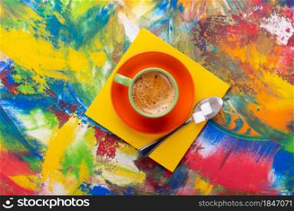 Cup of coffee and spoon with sugar at colorful abstract background texture. Coffee break time concept at abstract painting