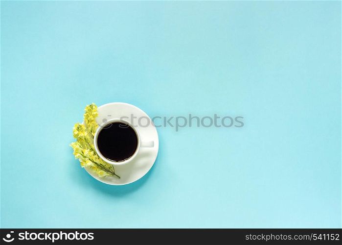 Cup of coffee and yellow wild flowers Linaria, blue paper background Flat lay Top view Concept Good morning or Hello spring Copy space Template for postcard, text or your design.. Cup of coffee and yellow wild flowers Linaria, blue paper background Flat lay Top view Concept Good morning or Hello spring Copy space Template for postcard, text or your design