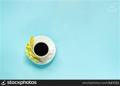 Cup of coffee and yellow wild flowers Linaria, blue paper background Flat lay Top view Concept Good morning or Hello spring Copy space Template for postcard, text or your design.. Cup of coffee and yellow wild flowers Linaria, blue paper background Flat lay Top view Concept Good morning or Hello spring Copy space Template for postcard, text or your design