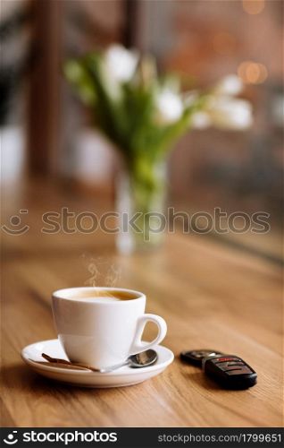 Cup of coffee, car remote key and vase of flowers on wooden table in coffee shop, selective focus. The concept of freelance. copy space.. Cup of coffee, car remote key and vase of flowers on wooden table in coffee shop, selective focus. The concept of freelance. copy space