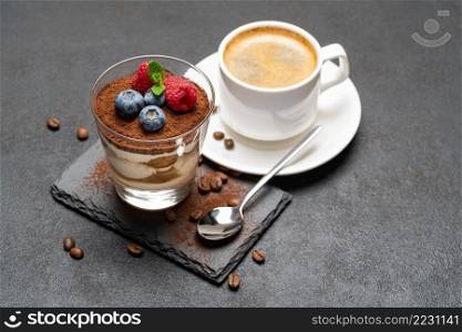 Cup of coffee Classic tiramisu dessert with blueberries and raspberries in a glass on stone serving board on dark concrete background or table. Cup of coffee Classic tiramisu dessert with blueberries and raspberries in a glass on stone serving board on dark concrete background