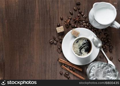 Cup of coffee, cream in a milk jug, glass of water and various spices on the wooden table with copy-space, top view