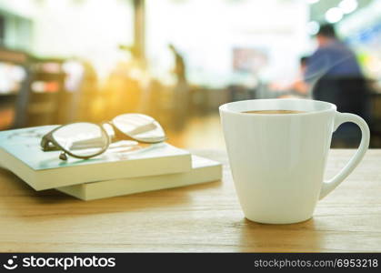 Cup of coffee, eyeglass and book on wooden table. Coffee break in morning, selective focus.