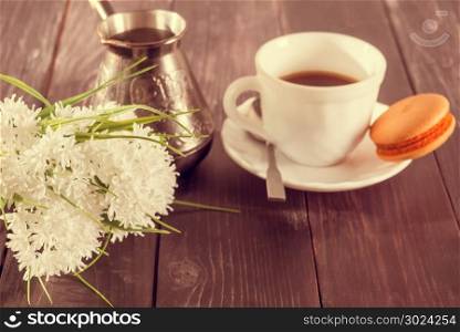 Cup of coffee, macaroni on a plate and a bouquet of flowers. Vintage processing