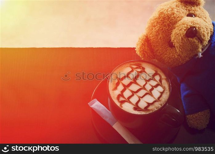 Cup of coffee next to Teddy Bear light orange.