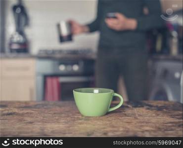 Cup of coffee on a table in a domestic kitchen with a man in the backround