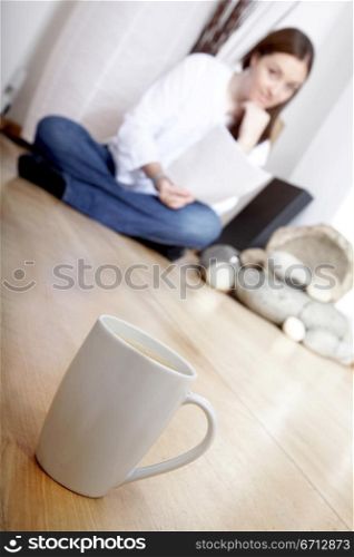cup of coffee on the floor with a woman reading a magazine at home in the background