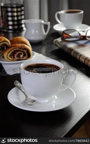 cup of coffee on the table with bread rolls and newspapers