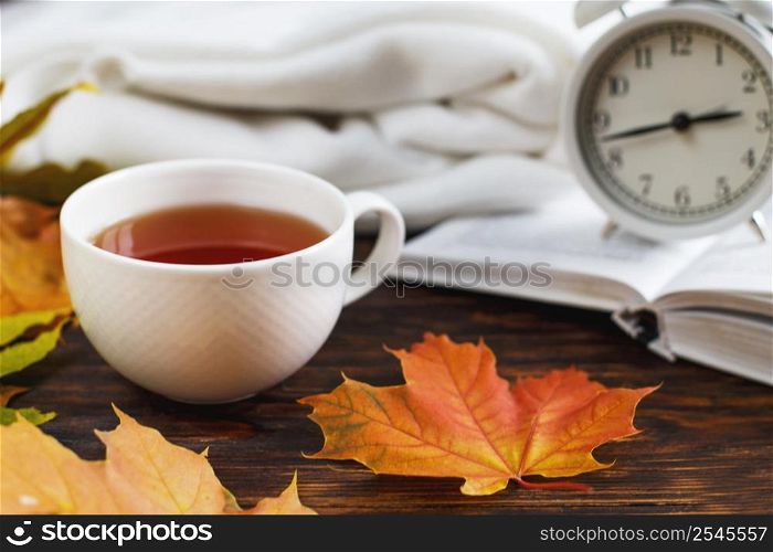 cup of coffee or tea with golden autumn leaves, plaid, alarm clock and book on a wooden background .top view. Fall concept. Autumn composition. cup of coffee or tea with golden autumn leaves, plaid, alarm clock and book on a wooden background .Fall concept.