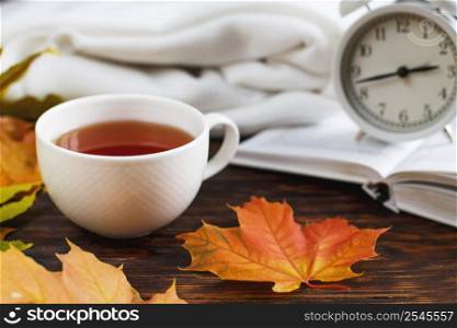cup of coffee or tea with golden autumn leaves, plaid, alarm clock and book on a wooden background .top view. Fall concept. Autumn composition. cup of coffee or tea with golden autumn leaves, plaid, alarm clock and book on a wooden background .Fall concept.