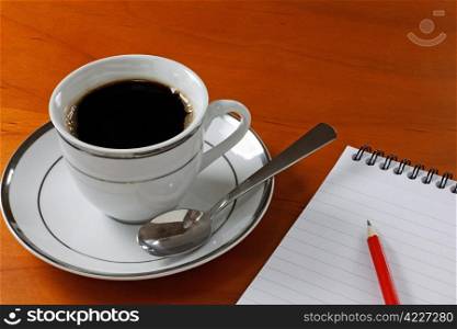 Cup of coffee with a notepad and pencil on a desk