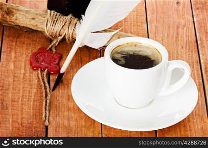 cup of coffee with a quill pen and ink scroll on wooden background