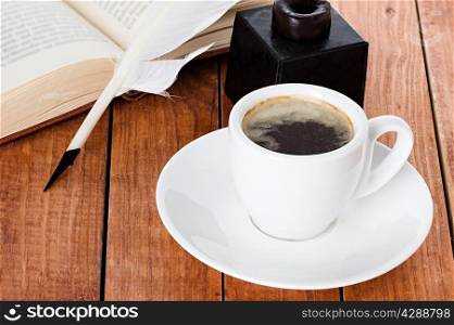 cup of coffee with a quill pen and inkwell on wooden background book