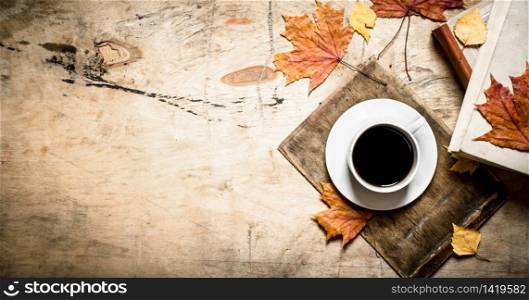 Cup of coffee with an old book and maple leaves. On wooden background.. Cup of coffee with an old book and maple leaves.