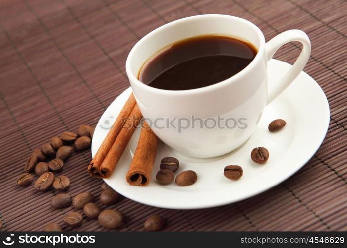 cup of coffee with cinnamon tubes and grains of coffee