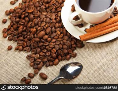 cup of coffee with cinnamon tubes and grains of coffee