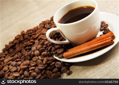 cup of coffee with cinnamon tubes and grains of coffee