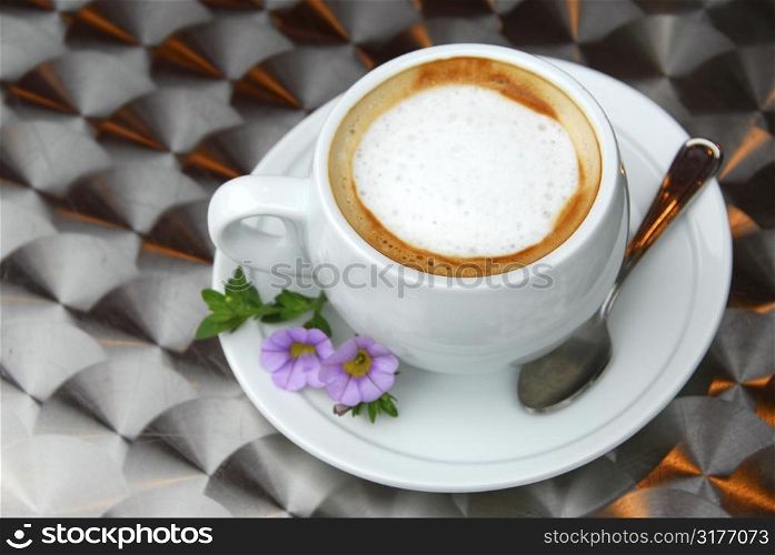 Cup of coffee with flowers on saucer on a table with metallic surface