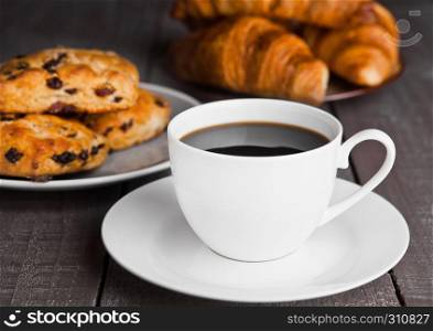 Cup of coffee with fresh scones and croissants on wooden table