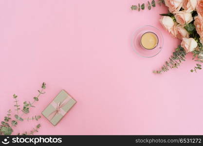 Cup of coffee with gift or present box and flowers on pink table from above, flat lay frame. Styled desktop scene. Styled desktop scene