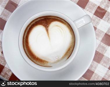 Cup of coffee with heart pattern in a white bowl on a checkered background