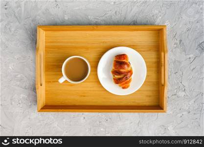 Cup of coffee with milk and freshly baked croissant on wooden tray on gray stone table. Concept Good morning Top view.. Cup of coffee with milk and freshly baked croissant on wooden tray on gray stone table. Concept Good morning Top view