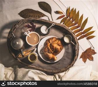 Cup of coffee with milk, jam and croissants on a tray with autumn leaves an early breakfast in bed, top view, selective focus