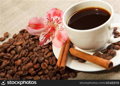 cup of coffee with tubes of cinnamon and a pink flower