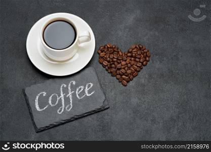 Cup of espresso and Heart shaped roasted coffee beans on dark concrete background.. Cup of espresso and Heart shaped roasted coffee beans on dark concrete background