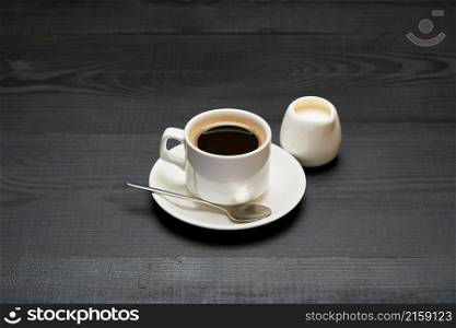 Cup of espresso coffee and pot of cream or milk on dark wooden background.. Cup of espresso coffee and pot of cream or milk on dark wooden background