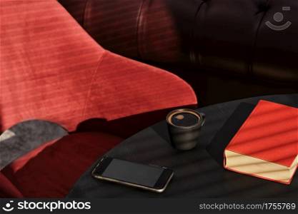 Cup of espresso on a black table, a red book and a red armchair, bright sunbeams on the table. Interior details of a cafe or loft studio