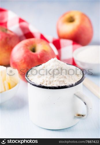 Cup of flour, butter, red apples and sugar. Ingredients for baking. Selective focus