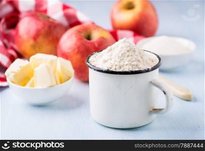 Cup of flour, butter, red apples and sugar. Ingredients for baking. Selective focus