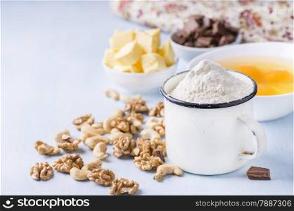 Cup of flour, eggs, butter, nuts and chocolate chunks. Ingredients for baking. Selective focus, copy space