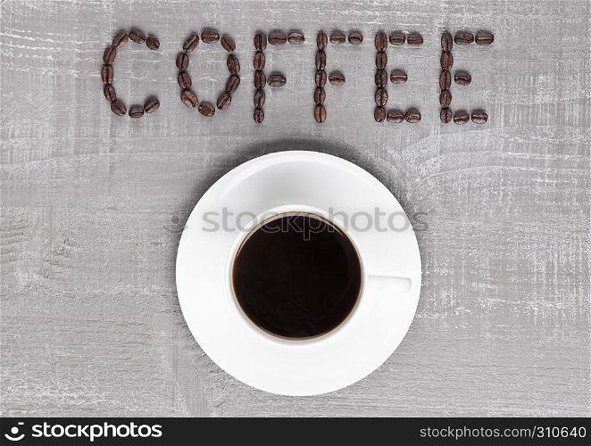 Cup of fresh coffee with sign made from beans on wooden background for cafe