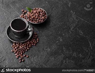 Cup of fresh raw organic coffee with beans and coffee tree leaf on black background. Black ceramic mug.