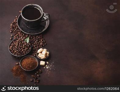 Cup of fresh raw organic coffee with beans and ground powder with cane sugar cubes with coffee tree leaf on dark background. Black ceramic mug