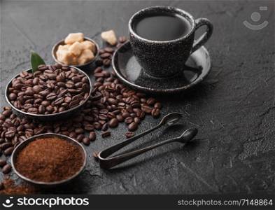 Cup of fresh raw organic coffee with beans and ground powder with cane sugar cubes with coffee tree leaf on dark background.