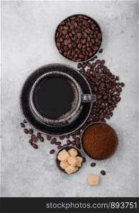 Cup of fresh raw organic coffee with beans and ground powder with cane sugar cubes with coffee tree leaf on light background.