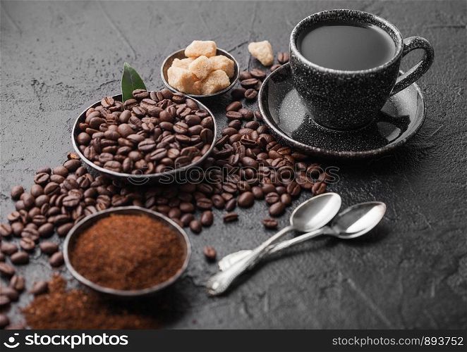Cup of fresh raw organic coffee with beans and ground powder with cane sugar cubes with coffee tree leaf on dark background.