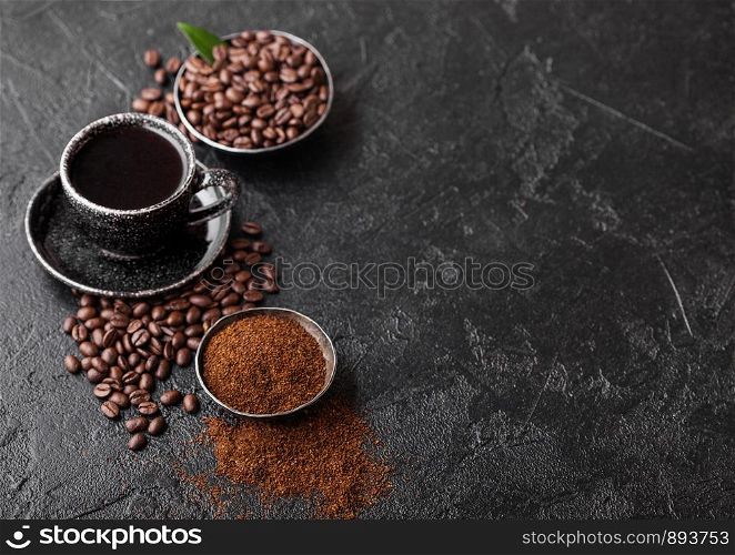 Cup of fresh raw organic coffee with beans and ground powder with coffee tree leaf on black background. Black ceramic mug