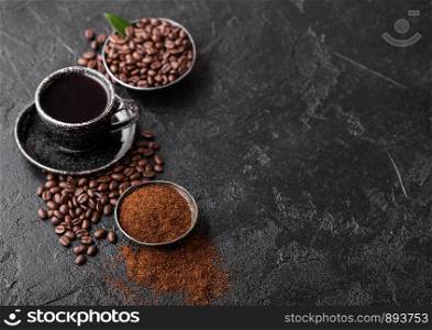 Cup of fresh raw organic coffee with beans and ground powder with coffee tree leaf on black background. Black ceramic mug