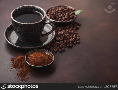 Cup of fresh raw organic coffee with beans and ground powder with cane sugar cubes with coffee tree leaf on dark background.